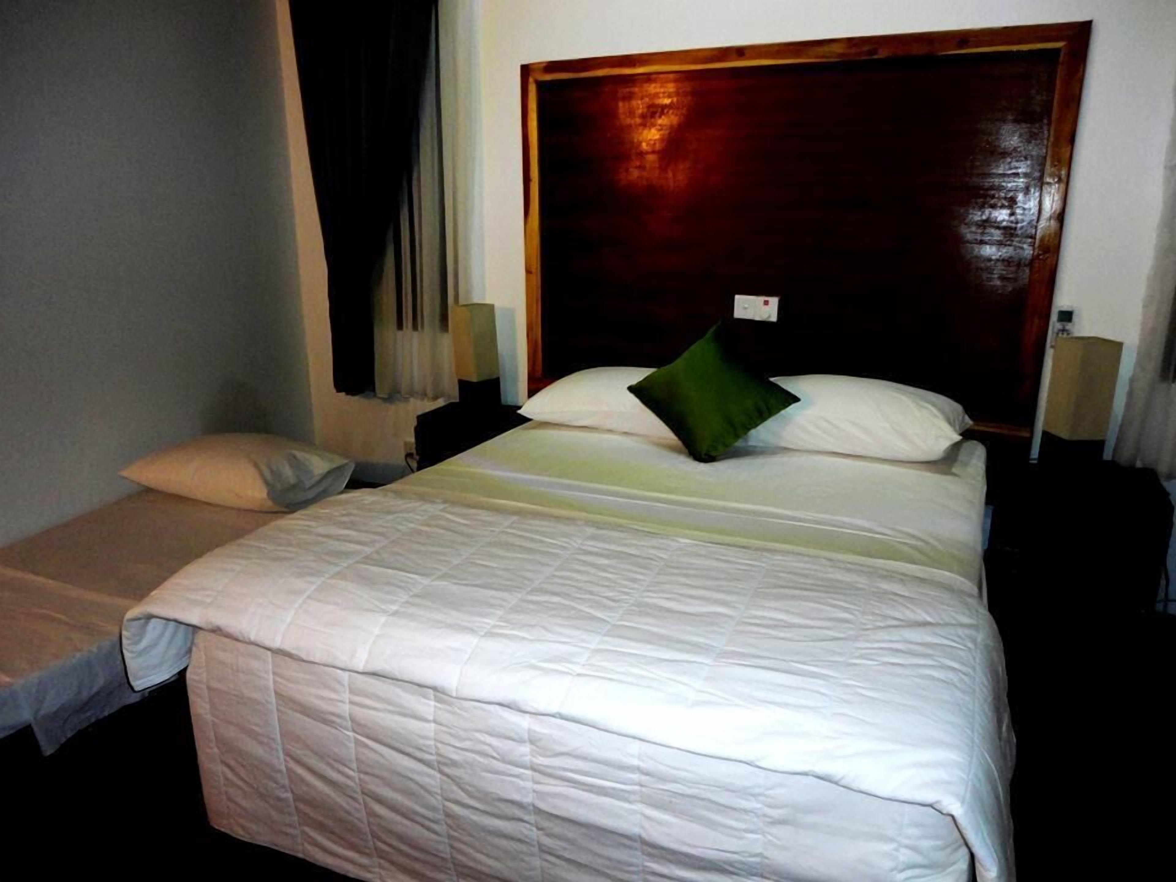 A hotel room with a large bed, a smaller bed, a wooden headboard, and a nightstand with a lamp.