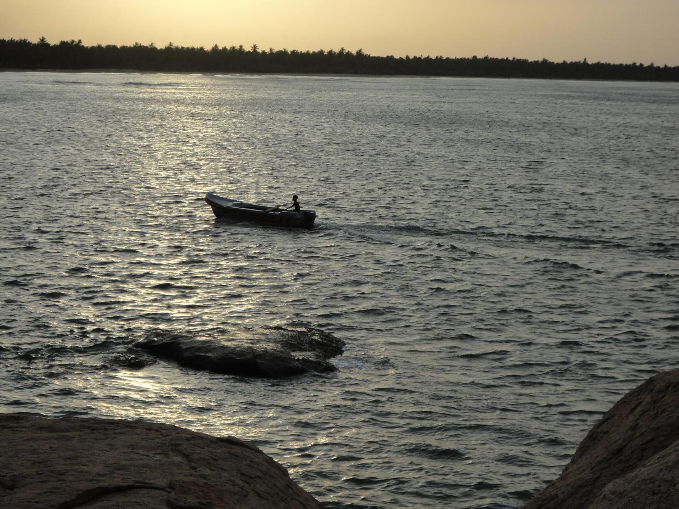 A calm body of water with a small boat and a person rowing.