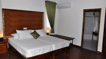 A double bed with white linens, a wooden headboard, a bedside table with a lamp, and a green curtain.