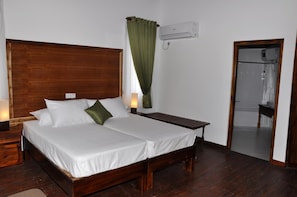 A double bed with white linens, a wooden headboard, a bedside table with a lamp, and a green curtain. - Hotel Naaval (Manmunai North)