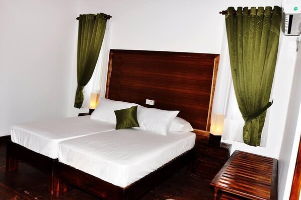 A double bed with white linens, two pillows, and green curtains.