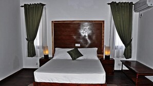 Una cama bien hecha con un cabecero de madera, dos mesitas de noche con lámparas y cortinas verdes.