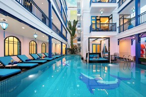 A hotel interior with a swimming pool, lounge chairs, and a staircase leading to upper floors. - Silk River Hoi An Retreat (Da Nang)