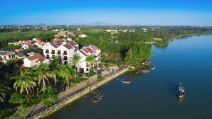 A riverside hotel with multiple buildings, a dock with boats, and a view of the surrounding landscape. - Silk River Hoi An Retreat (Da Nang)
