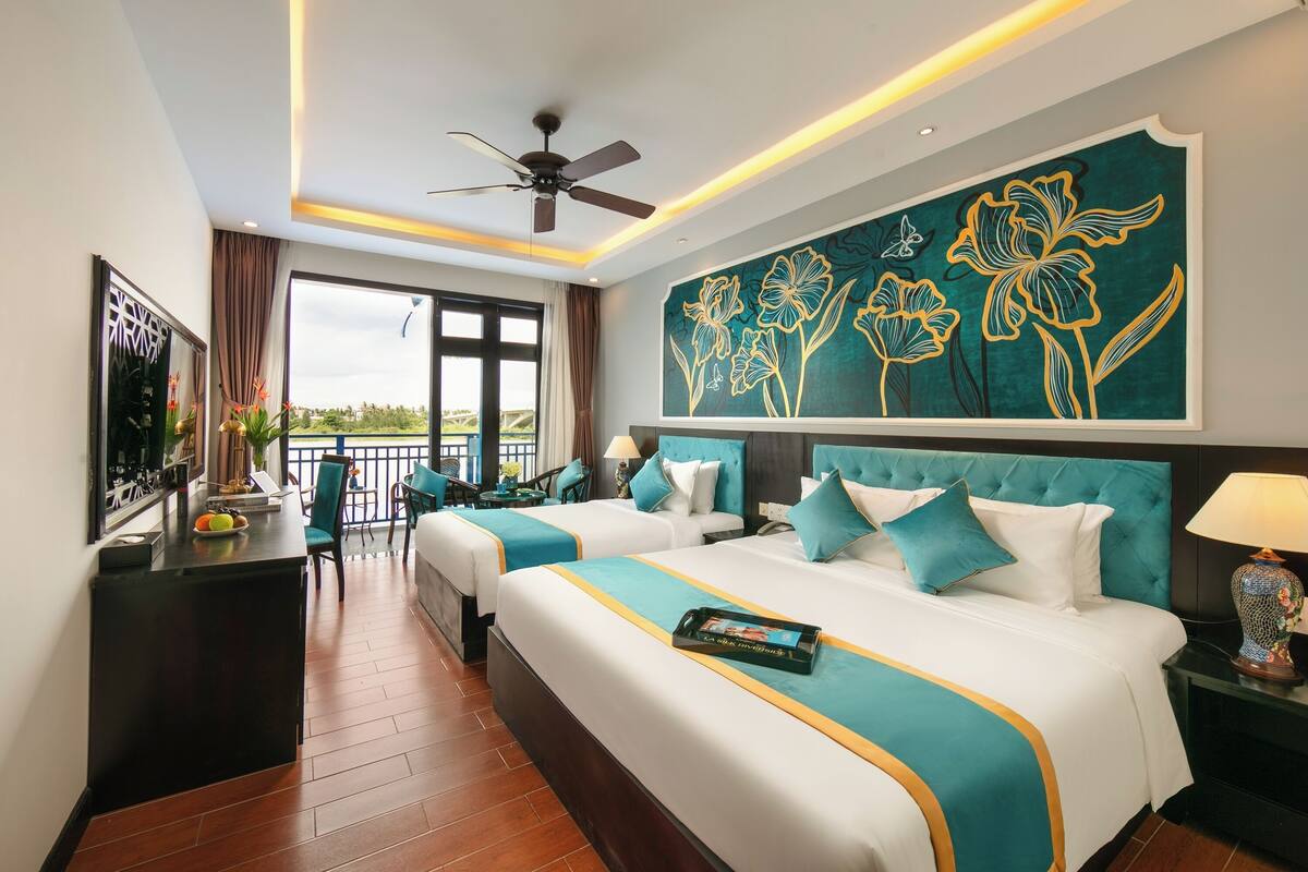 Habitación de hotel con dos camas, ventilador de techo, un gran cuadro floral en la pared y vistas al exterior.