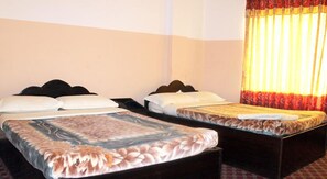 A hotel room with two single beds, each with a wooden headboard, white bedding, and a floral-patterned mattress cover. The room has plain walls and a window with yellow curtains. - Pashupati Plaza (Kathmandu)