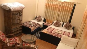A room with two beds, a wicker chair, a small round table, and a large wicker cabinet. - Cherry Garden (Pokhara)