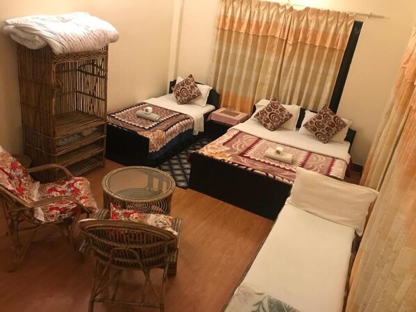 A room with two beds, a wicker chair, a small round table, and a large wicker cabinet. - Cherry Garden (Pokhara)