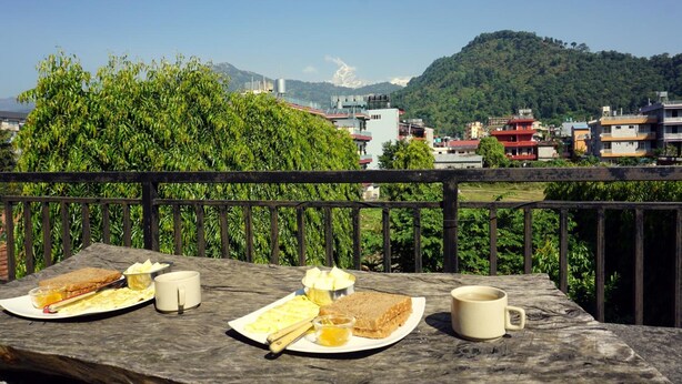 A wooden table with breakfast items and a view of a mountainous landscape. - Cherry Garden (Pokhara)