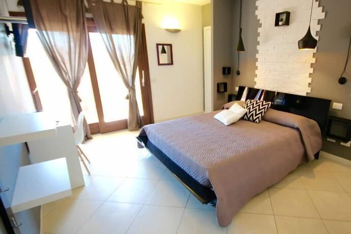 A bedroom with a bed, a desk, and a wall-mounted TV.