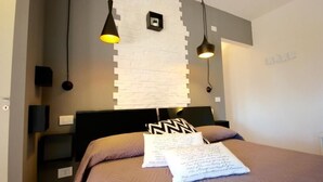 A modern bedroom with a bed, two bedside lamps, a white brick wall, and a small potted plant. - Park 20 Guesthouse (Olbia)