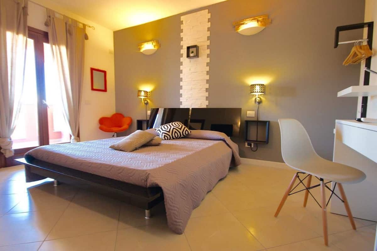 A modern bedroom with a bed, bedside lamps, a chair, and a desk.