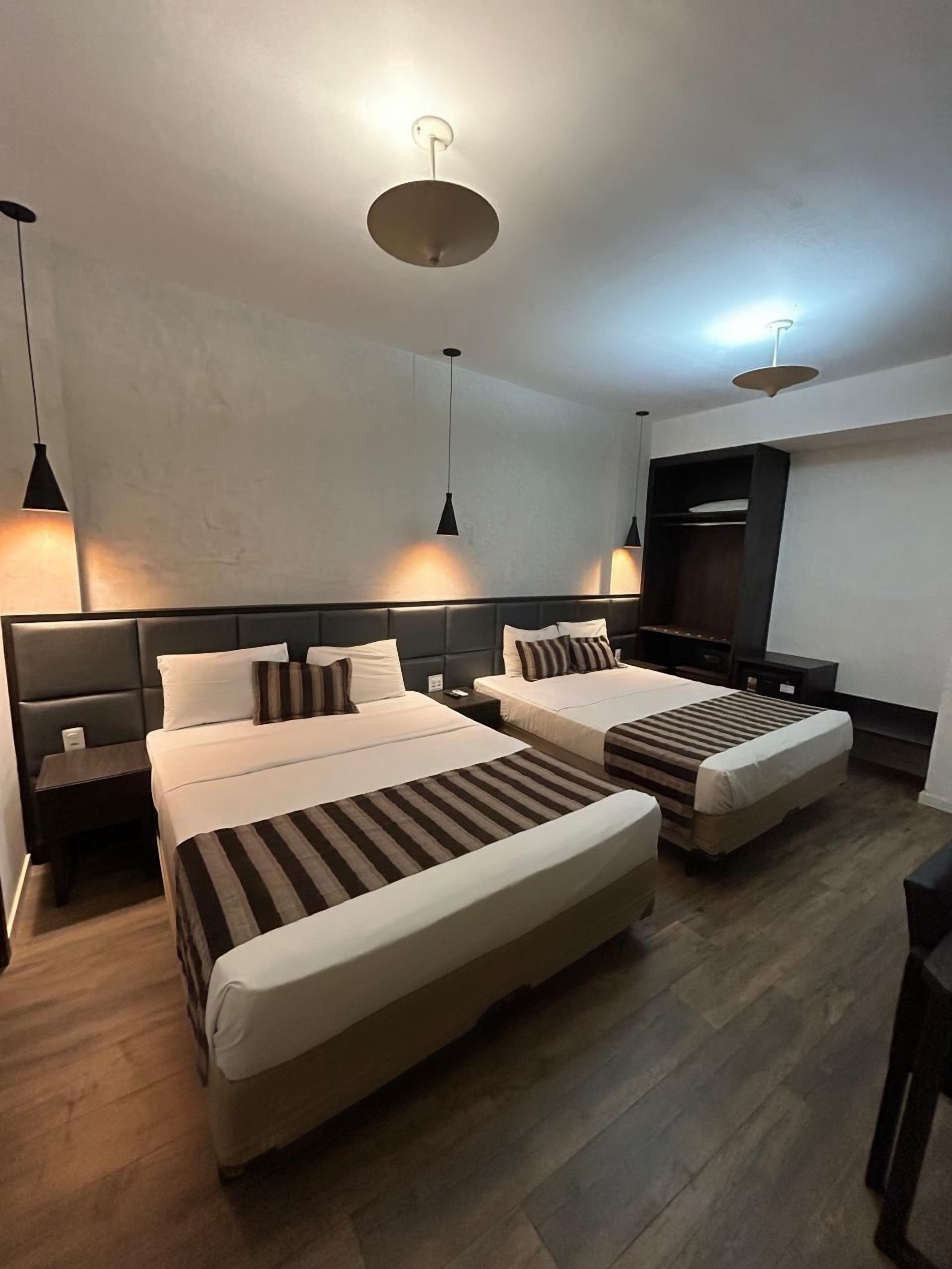 A modern hotel room with two beds, a dark headboard, and a built-in wardrobe.