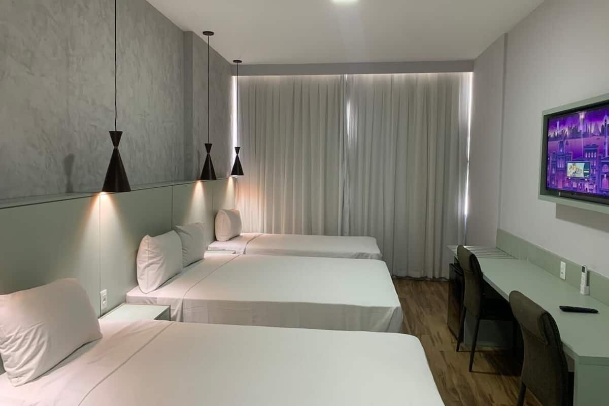 Een hotelkamer met twee eenpersoonsbedden, een bureau, een stoel, een televisie en een groot raam met gordijnen.