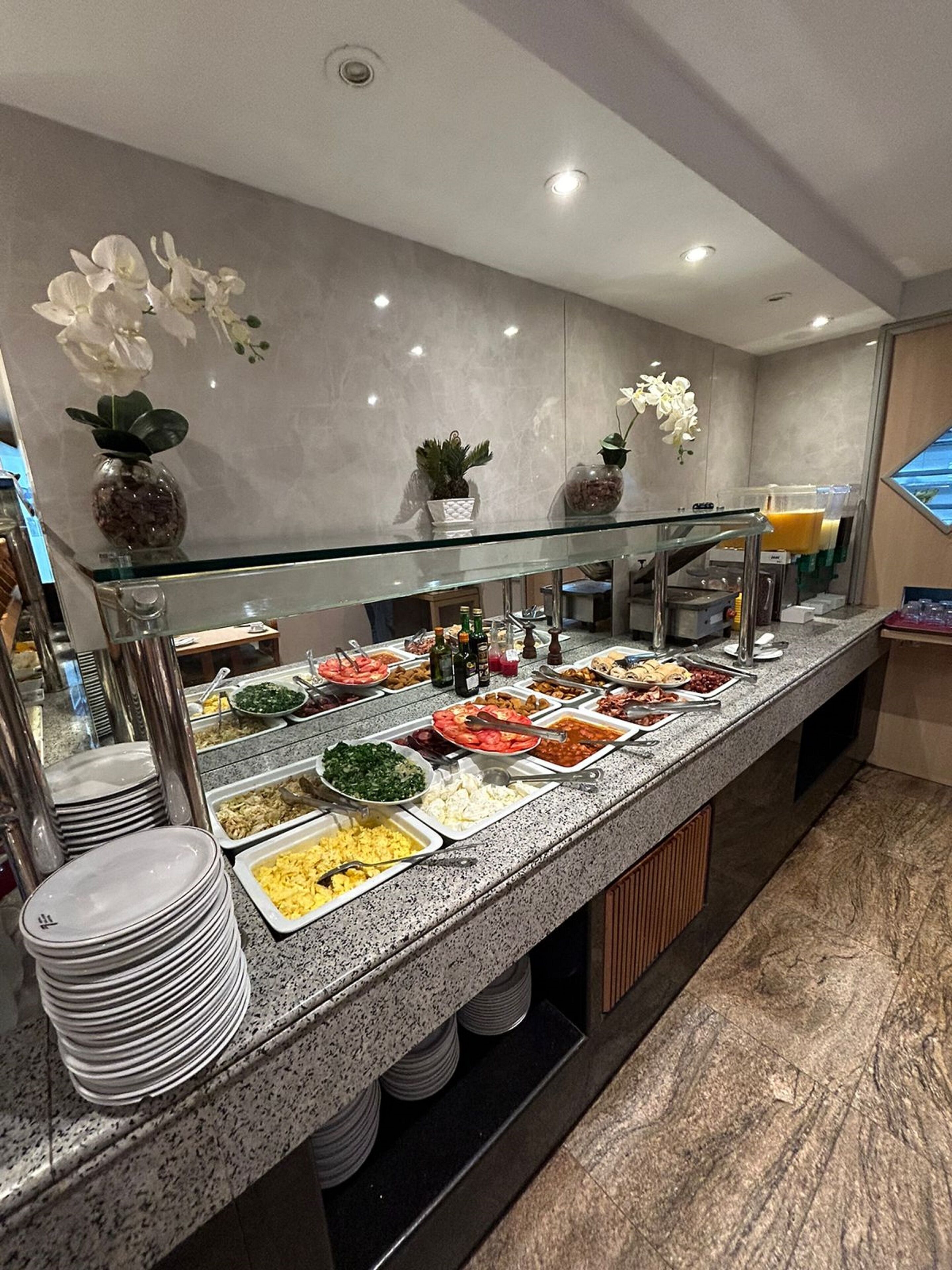 A buffet with various food options, a glass display case, and decorative plants.