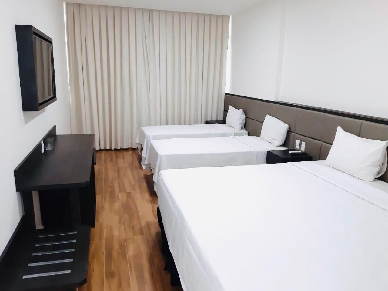 Une chambre d’hôtel avec deux lits simples, un bureau et un téléviseur fixé au mur.