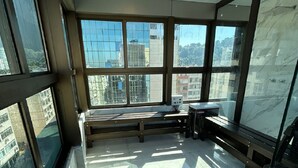 Habitación en un rascacielos con ventanales amplios, un banco y vistas a edificios de la ciudad.