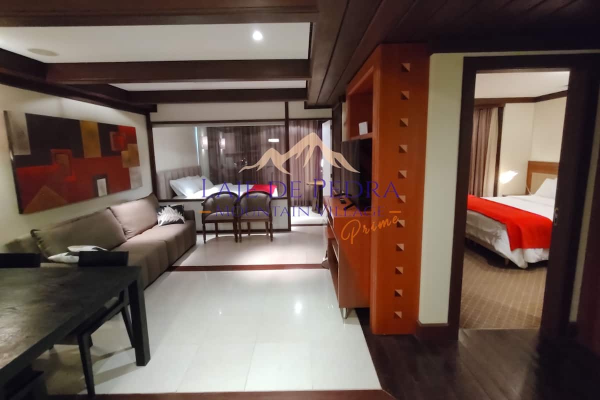 Una habitación de hotel moderna con sofá, mesa de comedor y cama con una manta roja.