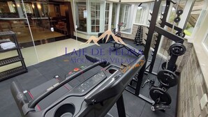 Een fitnessruimte met een loopband, krachttrainingsapparatuur en een spiegelwand.
