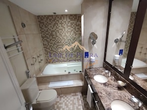 Un baño con bañera, dos lavamanos, un espejo grande y una zona de ducha con azulejos.