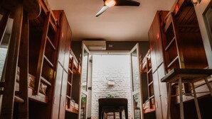 Un corridoio stretto con scaffali in legno su entrambi i lati, una ventola a soffitto e una porta aperta su un muro in mattoni.