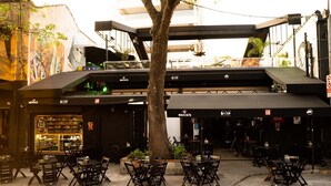 Zona esterna con tavoli e sedie, un albero e un edificio con insegne.
