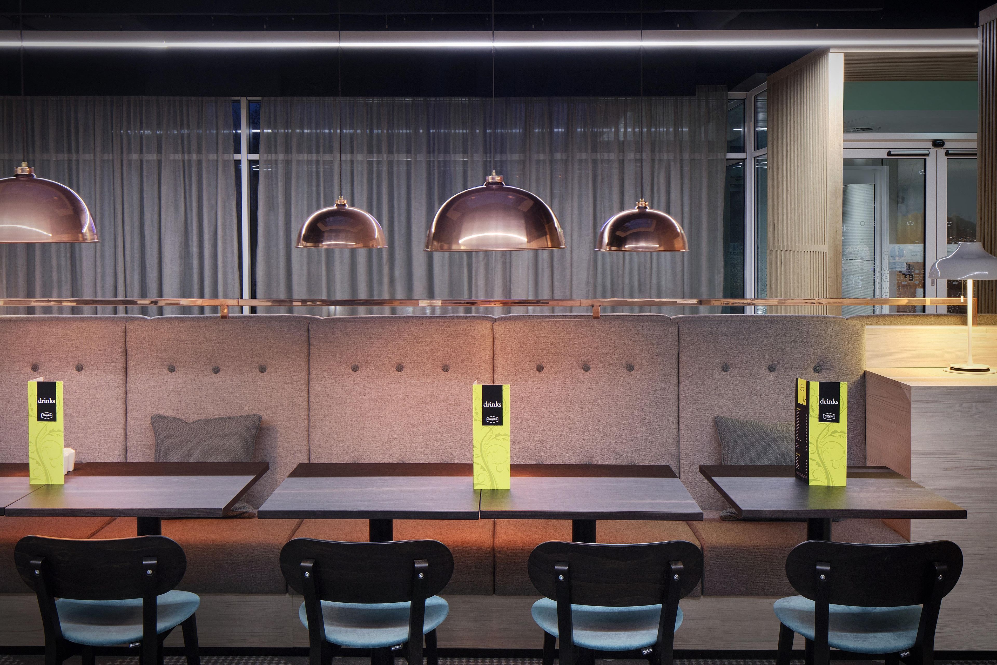 En modern restaurang med avskilda sittplatser, hängande lampor och ett menyställ.