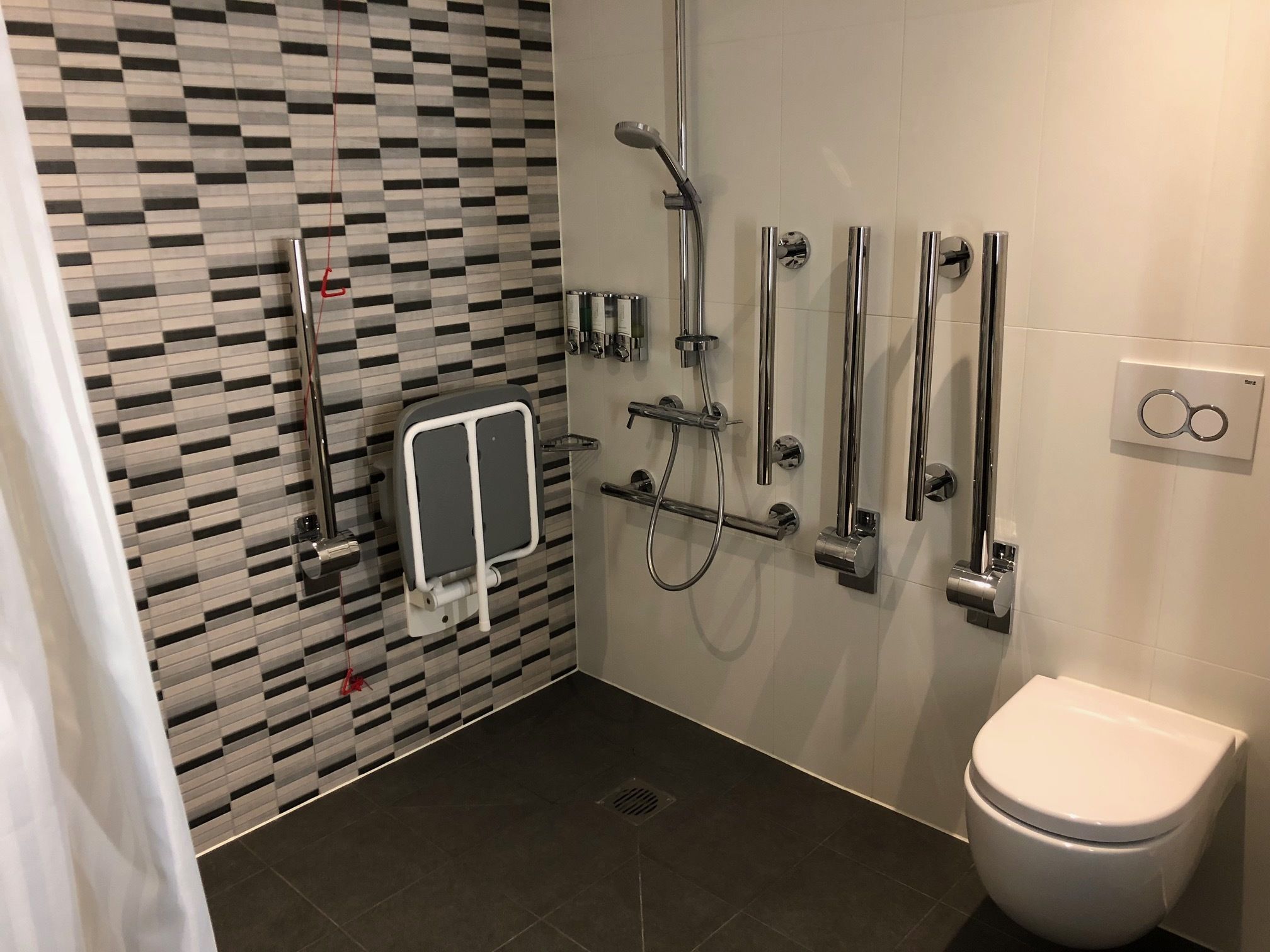 Ein modernes Badezimmer mit Wandfliesen im Schachbrettmuster, einer weißen Toilette und einer Dusche mit mehreren Bedienelementen.