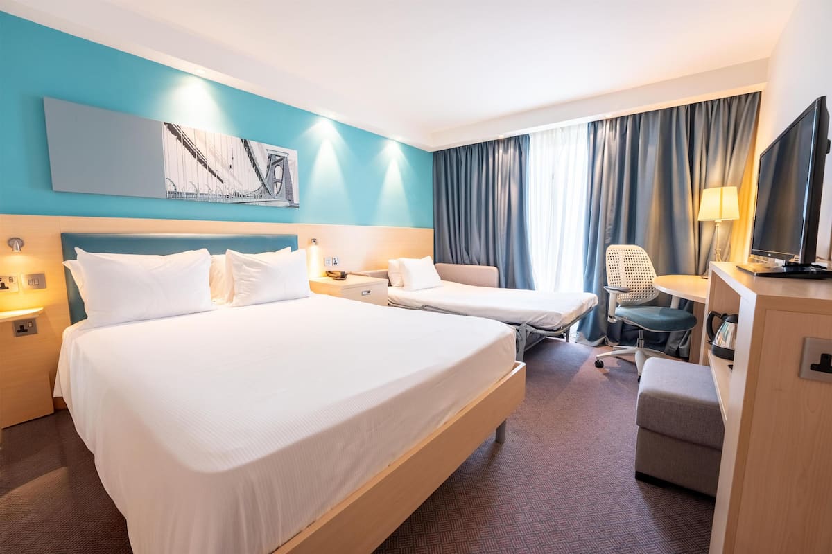 A hotel room with two beds, a desk, a chair, a TV, and a painting on the wall.