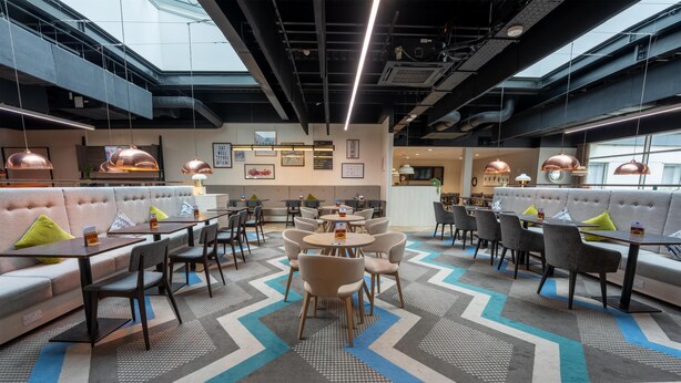 Um restaurante moderno com pé-direito alto, dutos aparentes e uma variedade de opções de assento, incluindo boxes e mesas.