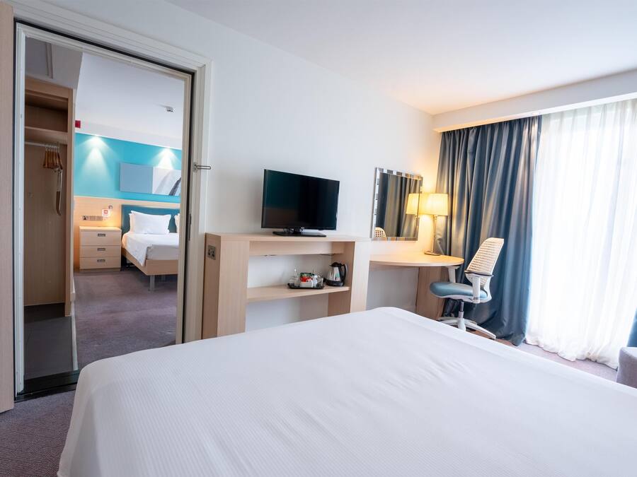 A hotel room with a bed, a desk, a television, a chair, a desk lamp, and a window with curtains.