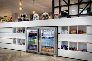 A modern retail space with refrigerated beverage dispensers, snack shelves, and hanging pendant lights.