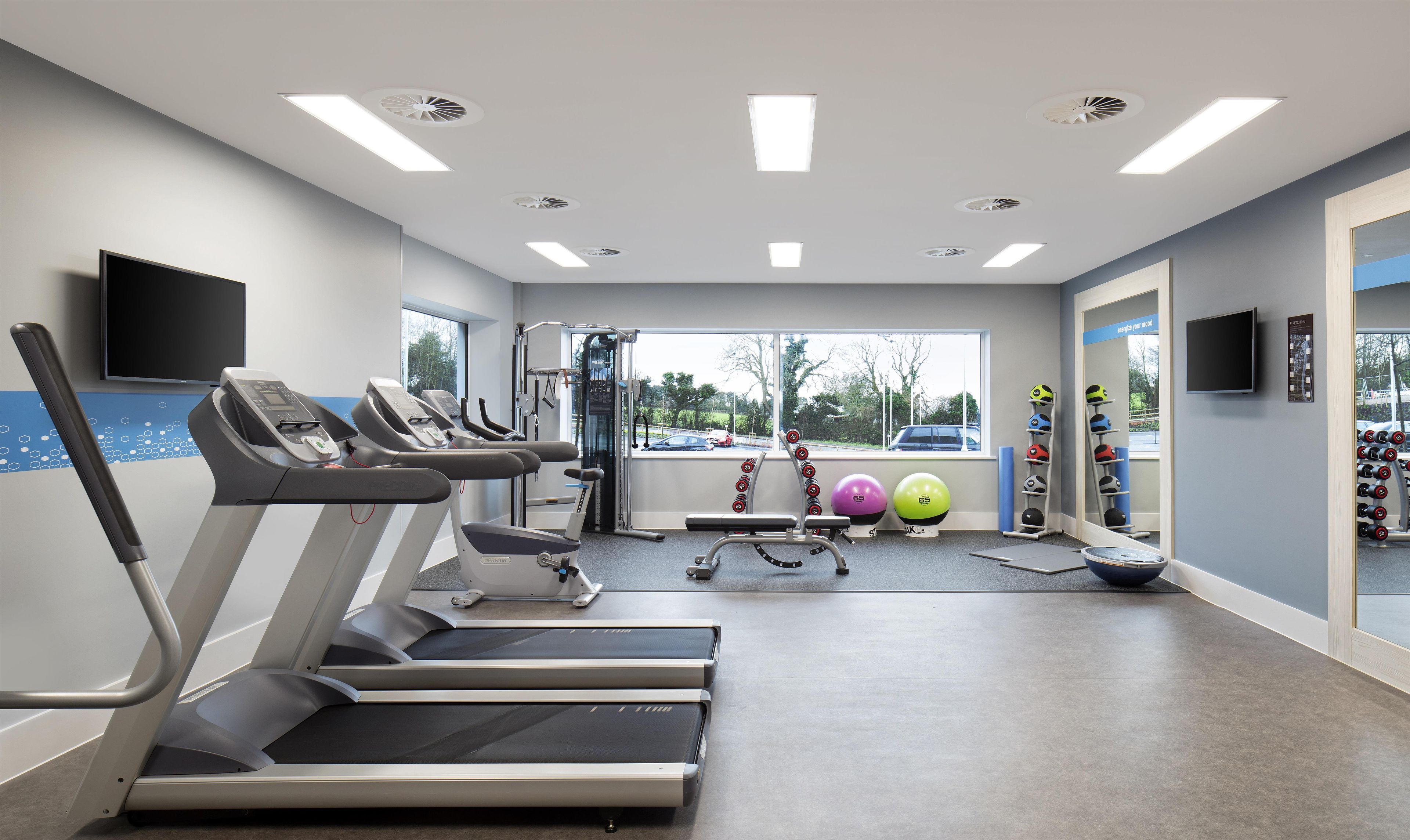 Un gimnasio con cintas de correr, pelotas de ejercicio y una pantalla de televisión.
