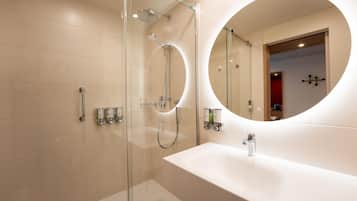 Un baño moderno con ducha envuelta en vidrio, un espejo redondo y un lavamanos blanco.