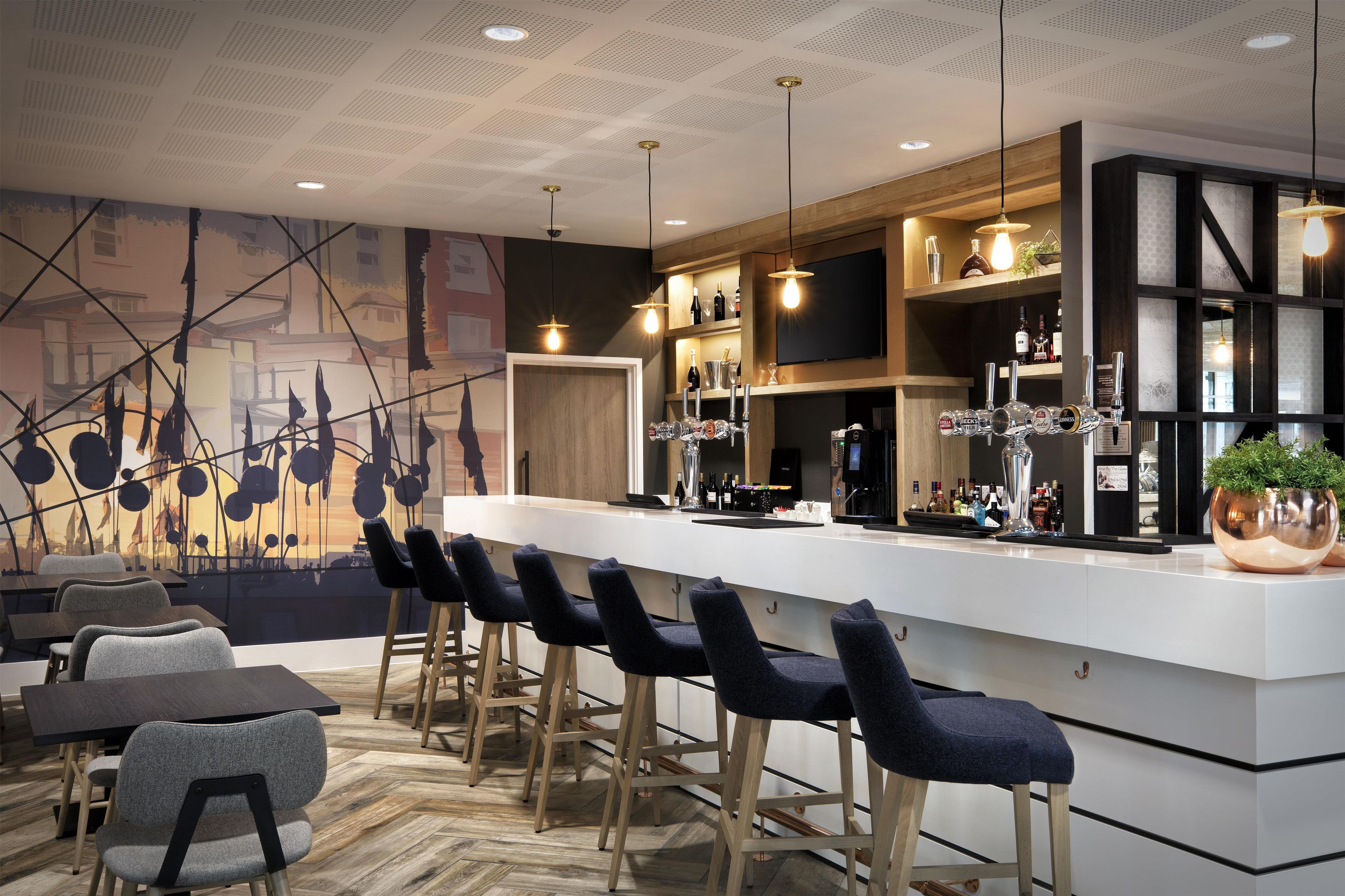 Un bar moderne doté d’un long comptoir, de nombreux tabourets et d’une grande variété de bouteilles et de verres.