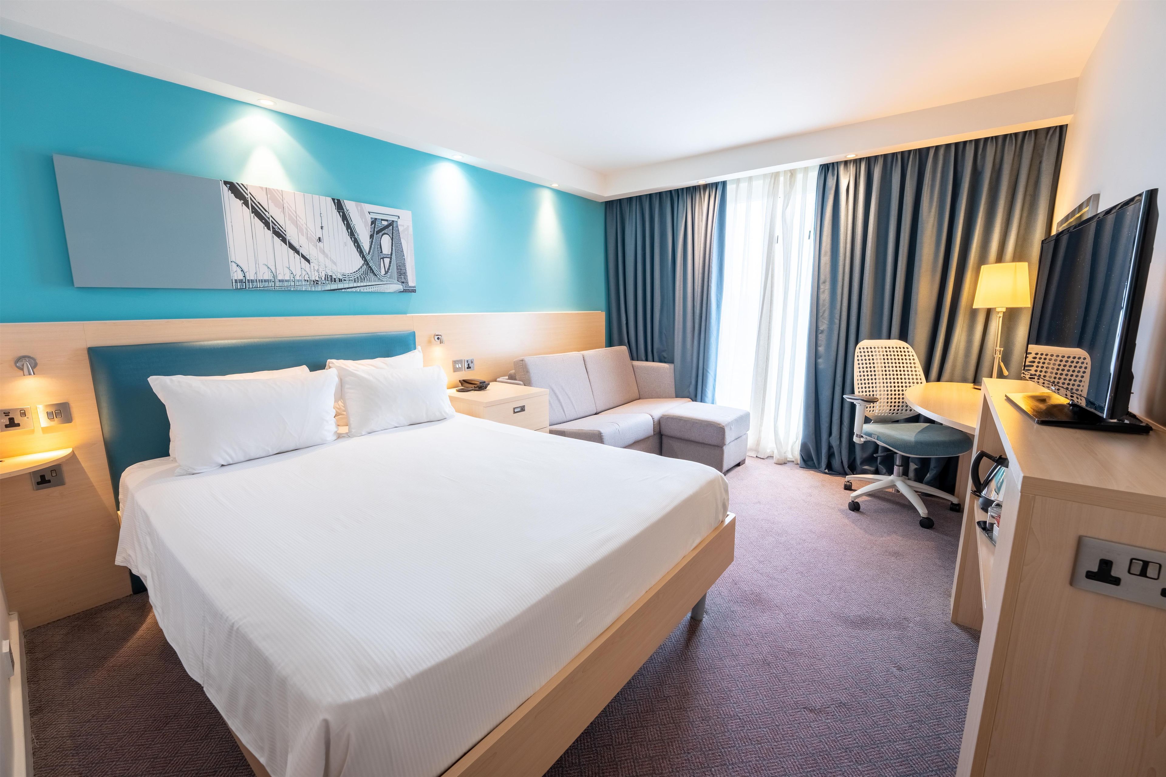 A hotel room with a large bed, a desk, a chair, and a television.