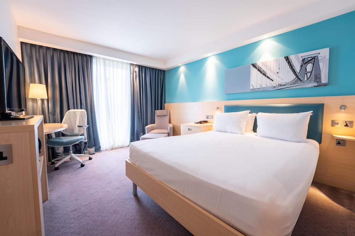A hotel room with a large bed, a desk with a chair, a TV, and a painting on the wall.