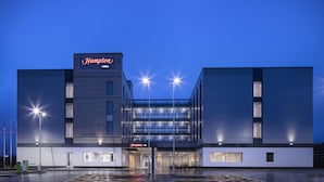 Um hotel moderno com um letreiro grande da Hampton, janelas amplas e estacionamento.