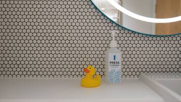A bathroom with a white sink, a yellow rubber duck, and a hand soap dispenser.