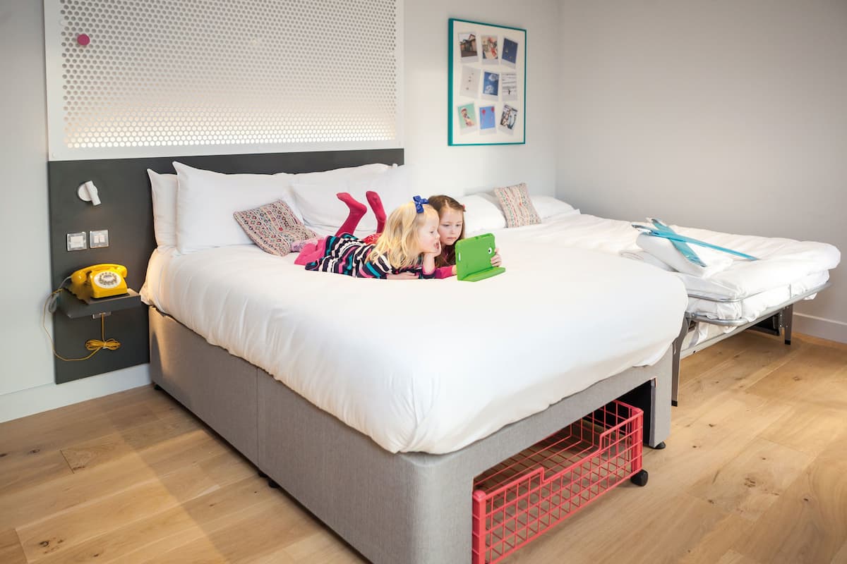 Quarto moderno com cama cinzenta, roupa de cama branca e mesa de cabeceira pequena com telefone amarelo.