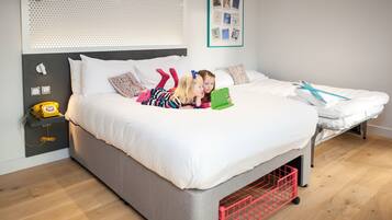 Un dormitorio moderno con una cama gris, ropa de cama blanca y una mesita de noche pequeña con un teléfono amarillo.