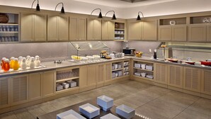 Une cuisine moderne avec des meubles de couleur beige, un buffet garni de plats et de boissons, et des assiettes soigneusement empilées sur le sol.