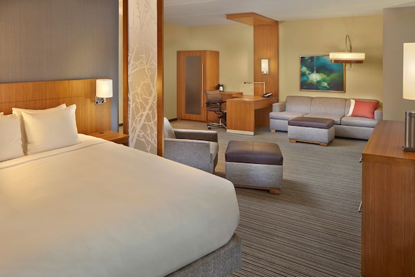 A hotel room with a large bed, a desk, a sofa, and a chair.