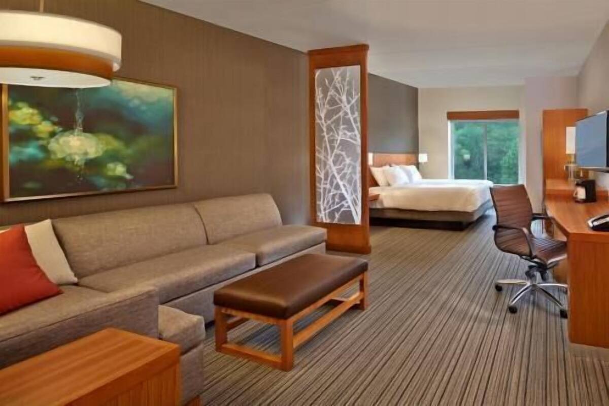 Ein Hotelzimmer mit einer Schlafcouch, einem Bett, einem Schreibtisch und einem großen Fenster.