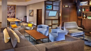 Un hall d’hôtel moderne avec un coin salon, un téléviseur et une bibliothèque.