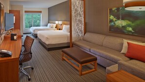 Une chambre d’hôtel équipée d’un bureau, de deux lits, d’un canapé, d’une banquette et d’une grande fenêtre.