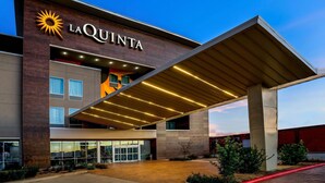 Una entrada de hotel moderna con un llamativo letrero de 'LAQUINTA', un paseo techado y un exterior bien iluminado.