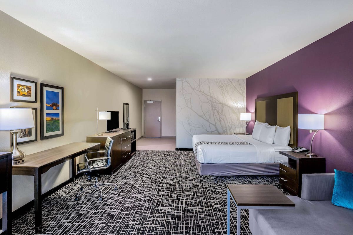 Une chambre d’hôtel avec un lit, un bureau, une chaise et une petite table. Une porte donne accès à une autre pièce.