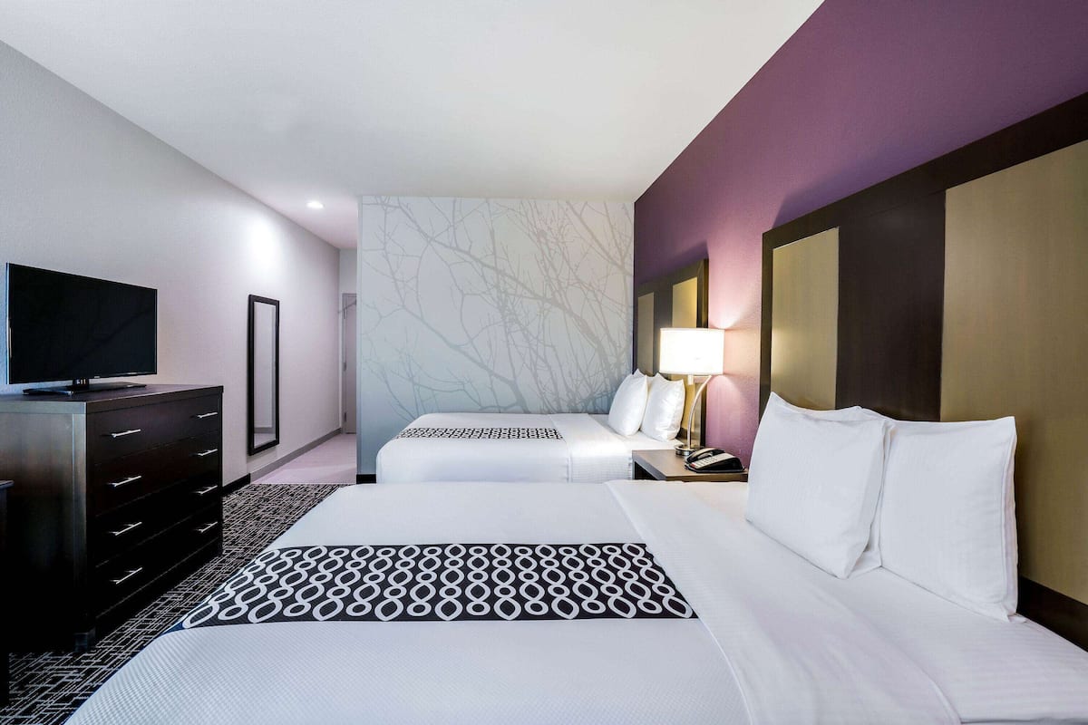 Une chambre d’hôtel avec deux lits, une télévision, une commode et une table de chevet avec une lampe.
