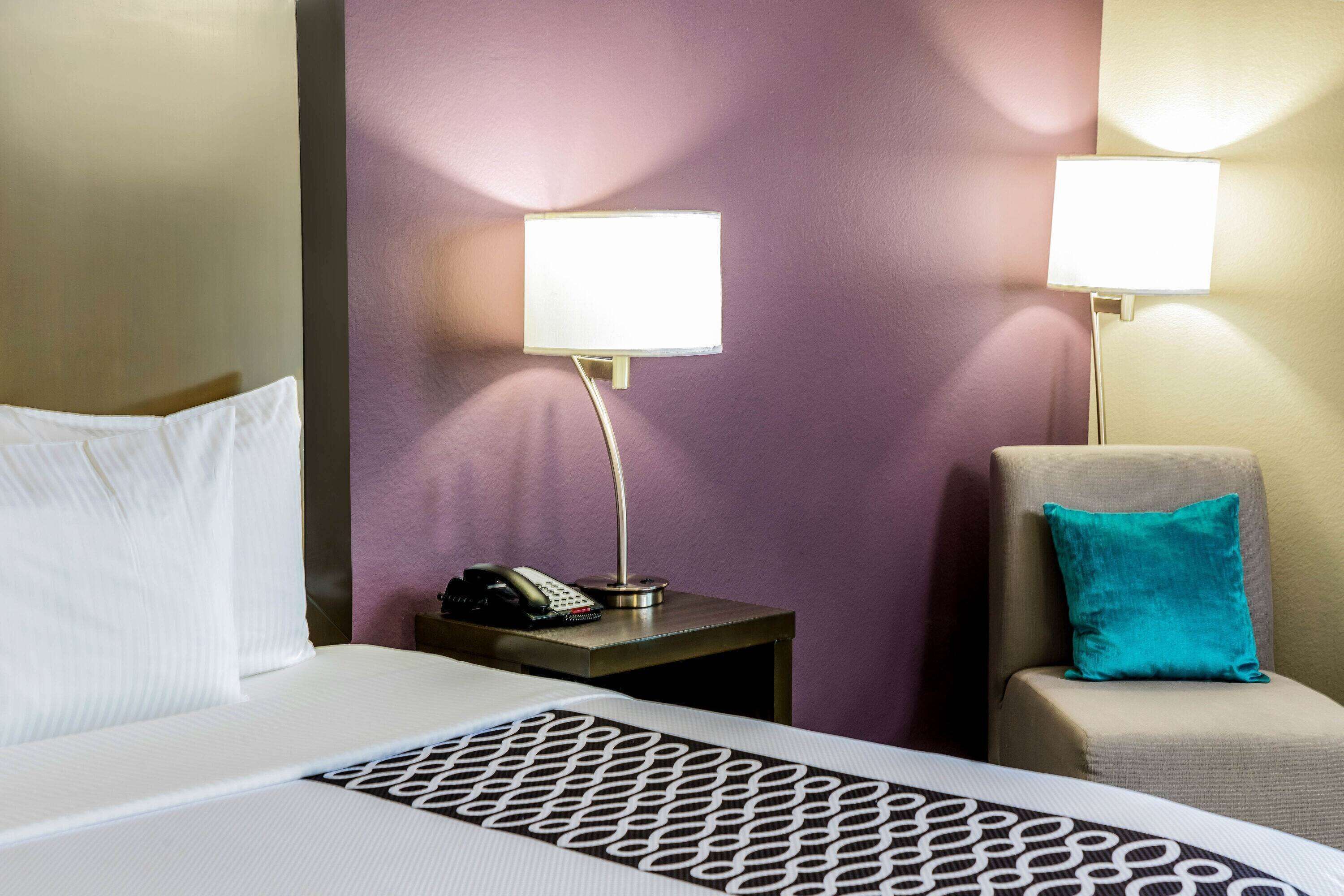 A hotel room with a bed, a nightstand with a phone, and two wall-mounted lamps.